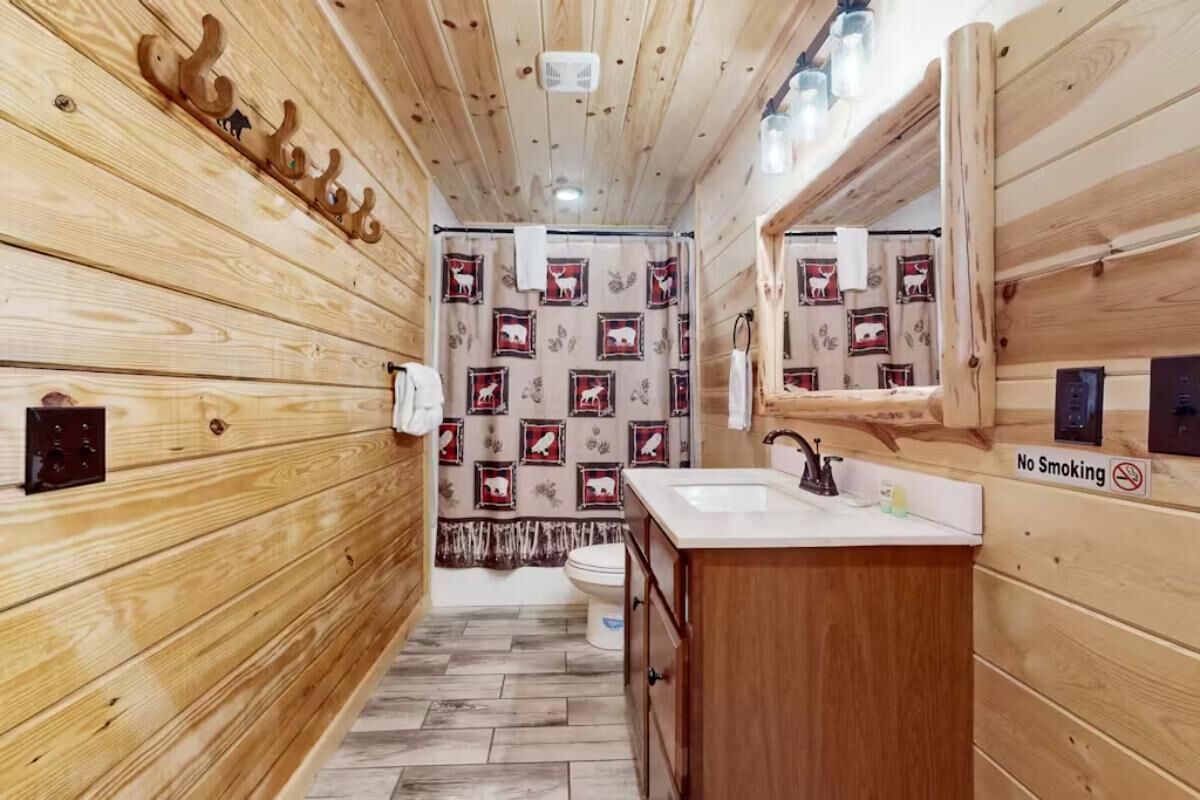 A wooden cabin-style bathroom with a wooden floor, a sink, a toilet, and a mirror.