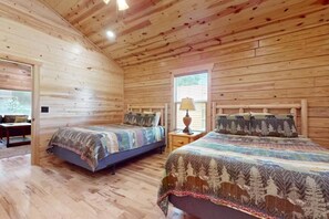 Ein Schlafzimmer in einer Blockhütte mit zwei Betten, einer Holzbalkendecke und einem Fenster.