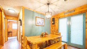 Un intérieur en bois avec une table à manger, des bancs, un luminaire suspendu et un tableau encadré au mur.