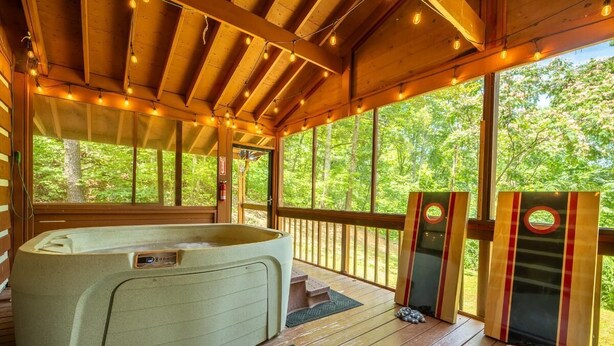 Une terrasse en bois avec un jacuzzi, de grandes fenêtres et une vue sur les arbres.