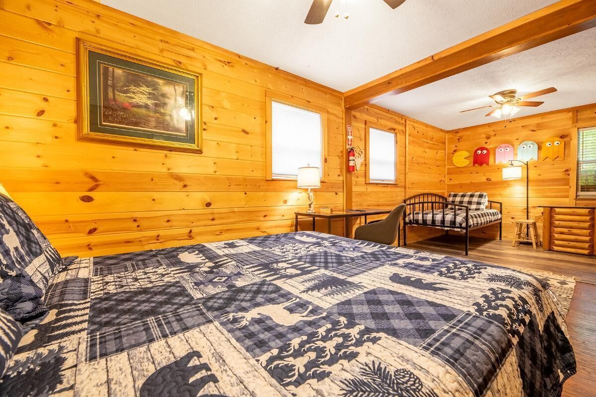 A log cabin room with a bed, a chair, a table, and a ceiling fan.