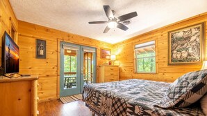 Une chambre dans une cabane en bois, avec un lit, un ventilateur de plafond, un bureau et une fenêtre.