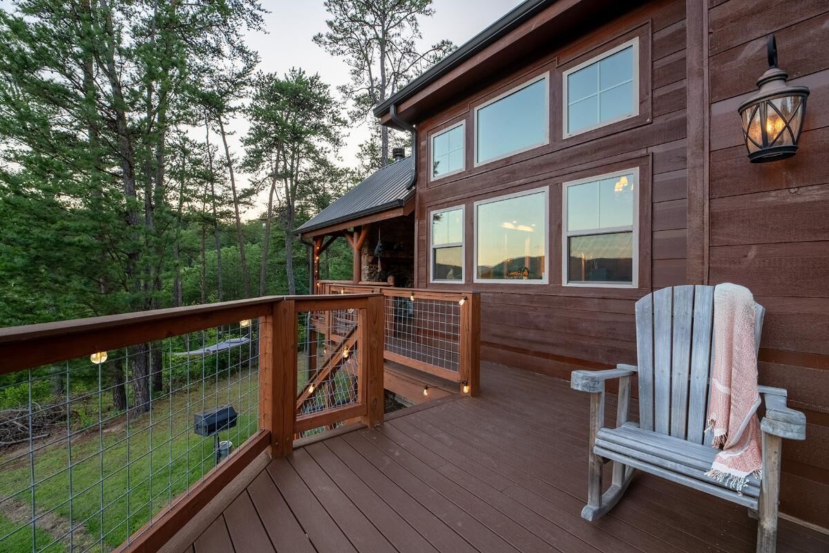 Una terraza de madera con una silla, barandilla y vistas a un bosque.