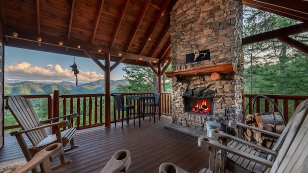 En täckt veranda med Adirondack-stolar, en steneldstad och en vacker utsikt över bergen.