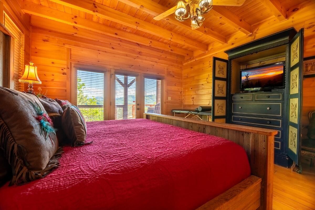 A wooden cabin room with a bed, a television, and a desk.