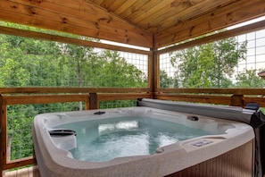 Ein Whirlpool in einer Holzhütte mit großen Fenstern und Blick auf Bäume.