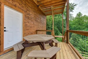 Eine Holzterrasse mit Tisch und Bänken, eine weiße Tür und Blick auf einen Wald.
