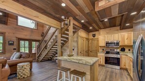 Interior de una cabaña con escalera de madera, cocina con electrodomésticos modernos, zona de bar y un rincón de estar acogedor.