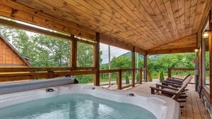 Una terraza de madera con un jacuzzi, sillas de madera y vistas a árboles y montañas.