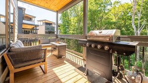 A covered outdoor deck with a grill, a cushioned bench, and a small table. - Smoky Mountain Sapphire (Pigeon Forge)