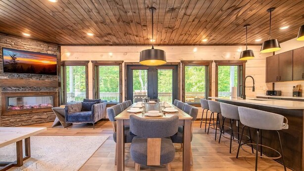 A spacious dining area with a wooden ceiling, a stone fireplace, and a large window. - Smoky Mountain Sapphire (Pigeon Forge)