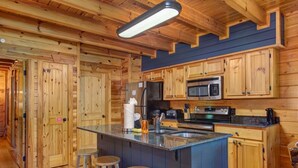 A wooden cabin interior with a kitchen featuring a central island, bar stools, and built-in appliances. - Goldilocks and The Three Bears (Gatlinburg)