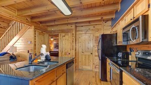 A wooden cabin interior with a kitchen area, a dining space, and a staircase. - Goldilocks and The Three Bears (Gatlinburg)
