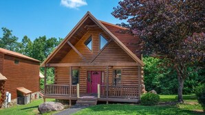 A log cabin with a front porch, a red door, and a small front yard. - Goldilocks and The Three Bears (Gatlinburg)