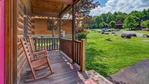 A wooden cabin with a porch, a grassy yard, and a view of a forested area. - Goldilocks and The Three Bears (Gatlinburg)