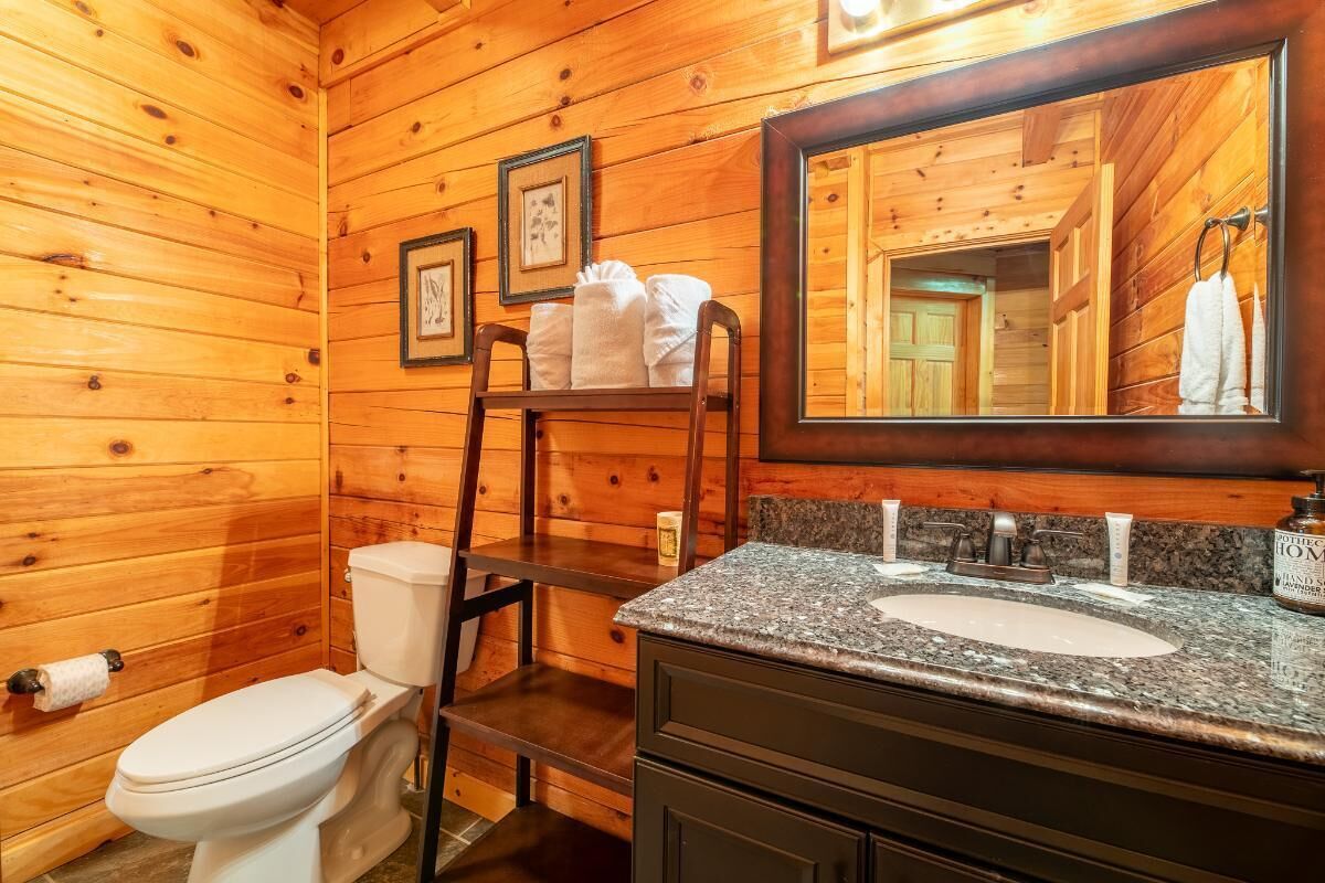 A wooden cabin bathroom with a toilet, sink, and a mirror.