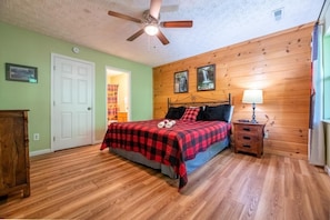 A bedroom with a bed, a ceiling fan, a wooden wall, and a door. - Z - Four Cubs Cottage (Sevierville)