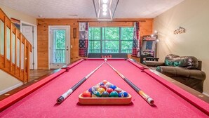 Ein Billardtisch mit Kugeln, eine Couch, ein Fernseher und ein Fenster mit Vorhängen.