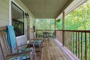 A wooden porch with a table and chairs, a bench with a towel, and a view of greenery. - Z - Four Cubs Cottage (Sevierville)