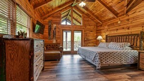 A wooden cabin bedroom with a bed, dresser, and a television on the wall. - Mountain Song (Gatlinburg)