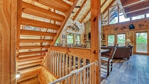 A wooden interior with a staircase, a dining area, and a living room with a stone wall and windows. - Mountain Song (Gatlinburg)