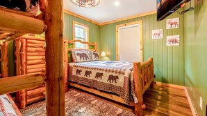 A log cabin-style room with a bed, wooden walls, a chandelier, a TV, and animal-themed decor. - Oldham Ridge Retreat (Sevierville)