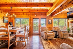 A wooden cabin interior with a dining area, two reclining chairs, a fireplace, and a television. - Sharp Dressed Bear (Sevierville)