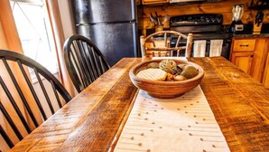 Una mesa de madera para comer con una cesta trenzada que contiene varios objetos, un mantel individual estampado y sillas negras.