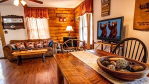 Una habitación acogedora de estilo cabaña con una mesa de comedor de madera, un sofá con cojines estampados, un televisor y un reloj de pared.
