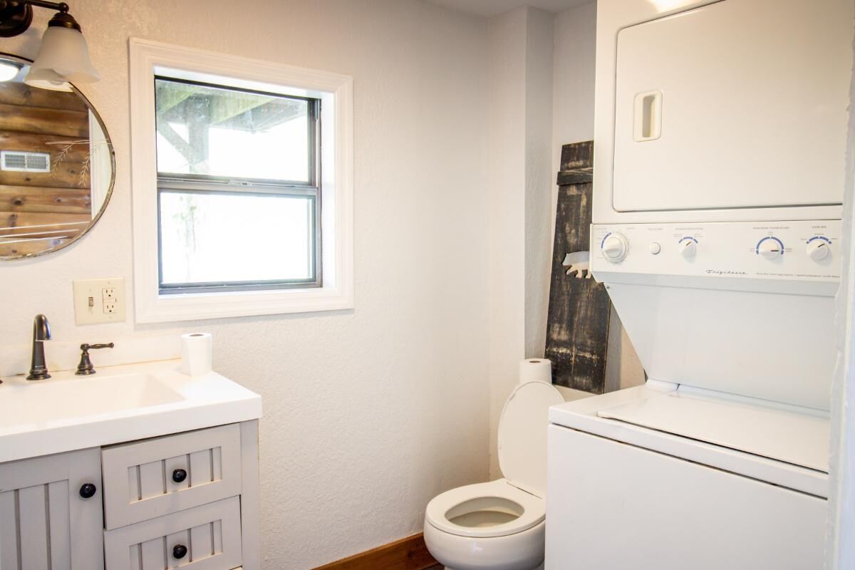 A bathroom with a white sink, a toilet, and a stacked washer and dryer.