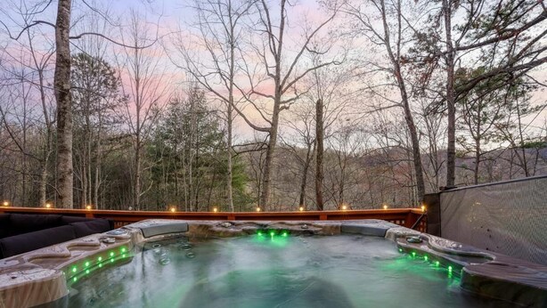 A hot tub surrounded by trees, with a wooden deck and a view of the landscape. - Smoky Fox Lodge (Sevierville)