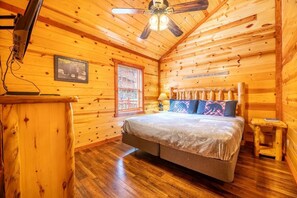 A wooden cabin bedroom with a bed, a ceiling fan, a window, and a sign on the wall. - Splash Mountain Lodge (Sevierville)