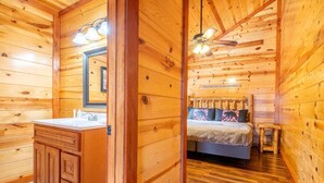 Ein Holzblockhaus-Interieur mit Bad, Bett und Deckenventilator.