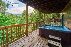 En træterrasse med jacuzzi, trægelændere og udsigt til et skovområde.