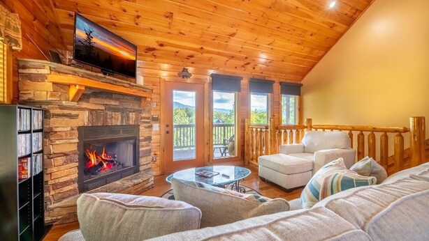 A cozy interior with a stone fireplace, wooden ceiling, and a balcony with outdoor furniture. - Simply Heaven in the Smokies (Sevierville)