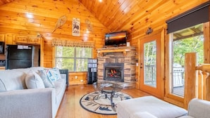 A log cabin interior with a fireplace, two sofas, a dining table, and a bookshelf. - Simply Heaven in the Smokies (Sevierville)