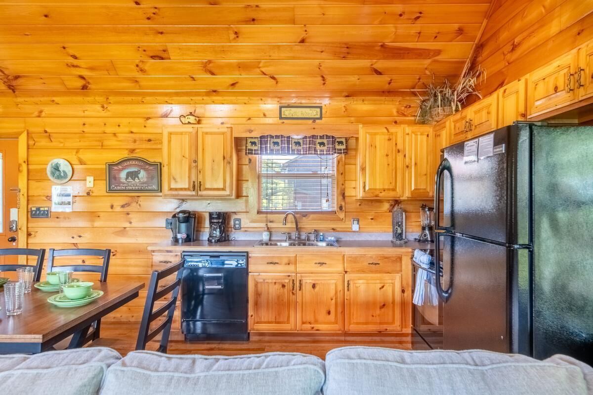 A cabin-style kitchen with wooden walls and a black refrigerator.