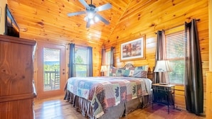 A wooden cabin bedroom with a bed, two lamps, a ceiling fan, and a door leading outside. - Simply Heaven in the Smokies (Sevierville)