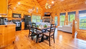 A wooden cabin interior with a dining area, kitchen, and a sofa by a large window. - Simply Heaven in the Smokies (Sevierville)