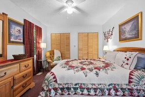 A bedroom with a bed, a dresser, a chair, a ceiling fan, and two doors. - Mountain Dew (Gatlinburg)