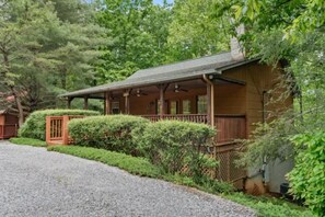A wooden cabin with a porch, surrounded by dense greenery and trees. - Mountain Dew (Gatlinburg)