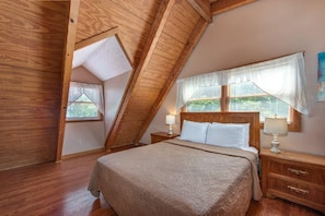 A bedroom with a sloped ceiling, a bed with a headboard, bedside lamps, and a window with blinds. - Paradise (Gatlinburg)