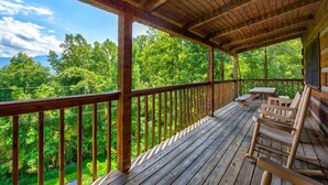 A wooden deck with a view of a forest, a picnic table, and two rocking chairs. - Paradise (Gatlinburg)