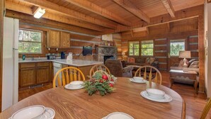 A wooden cabin interior with a dining table set for four, a kitchen area, and a cozy living space with a fireplace. - Paradise (Gatlinburg)