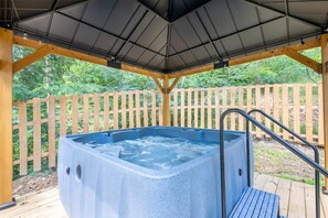 Ein Whirlpool unter einer Holzpergola mit Metalldach, umgeben von Holzzaun und Grünpflanzen.