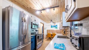 Una cocina moderna con electrodomésticos de acero inoxidable, techo de madera y un comedor con sillas amarillas.