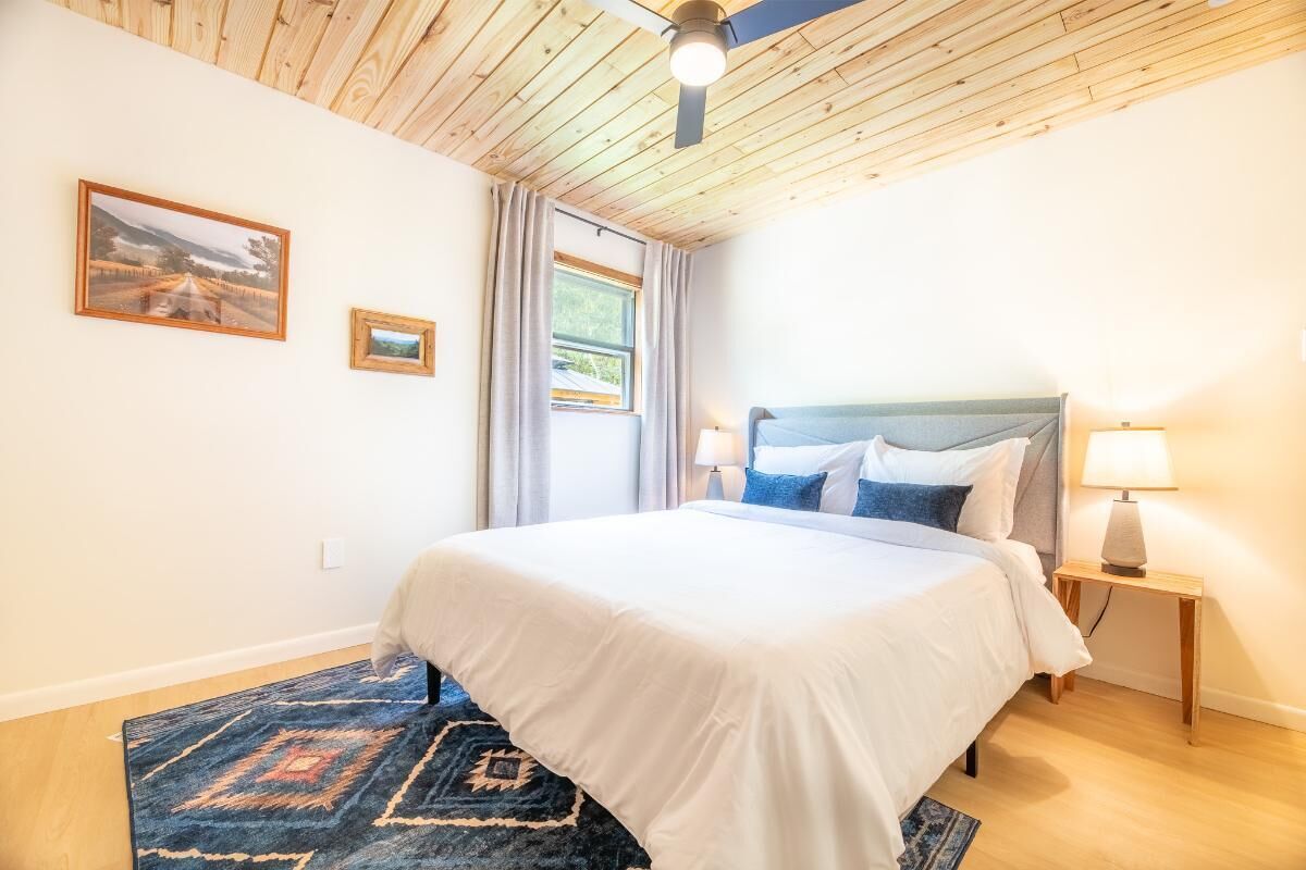 A bedroom with a bed, a ceiling fan, a window with curtains, and two wall-mounted lamps.