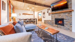 Una sala de estar acogedora con chimenea, un televisor montado en una pared de piedra y un comedor al fondo.