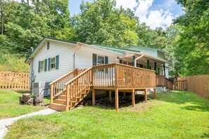 Ein Bungalow mit einer Holzterrasse, einer Treppe zum Veranda und einem umzäunten Garten.