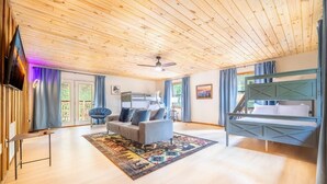 Habitación con techo de madera, un sofá, una cama, un televisor y una ventana con cortinas.